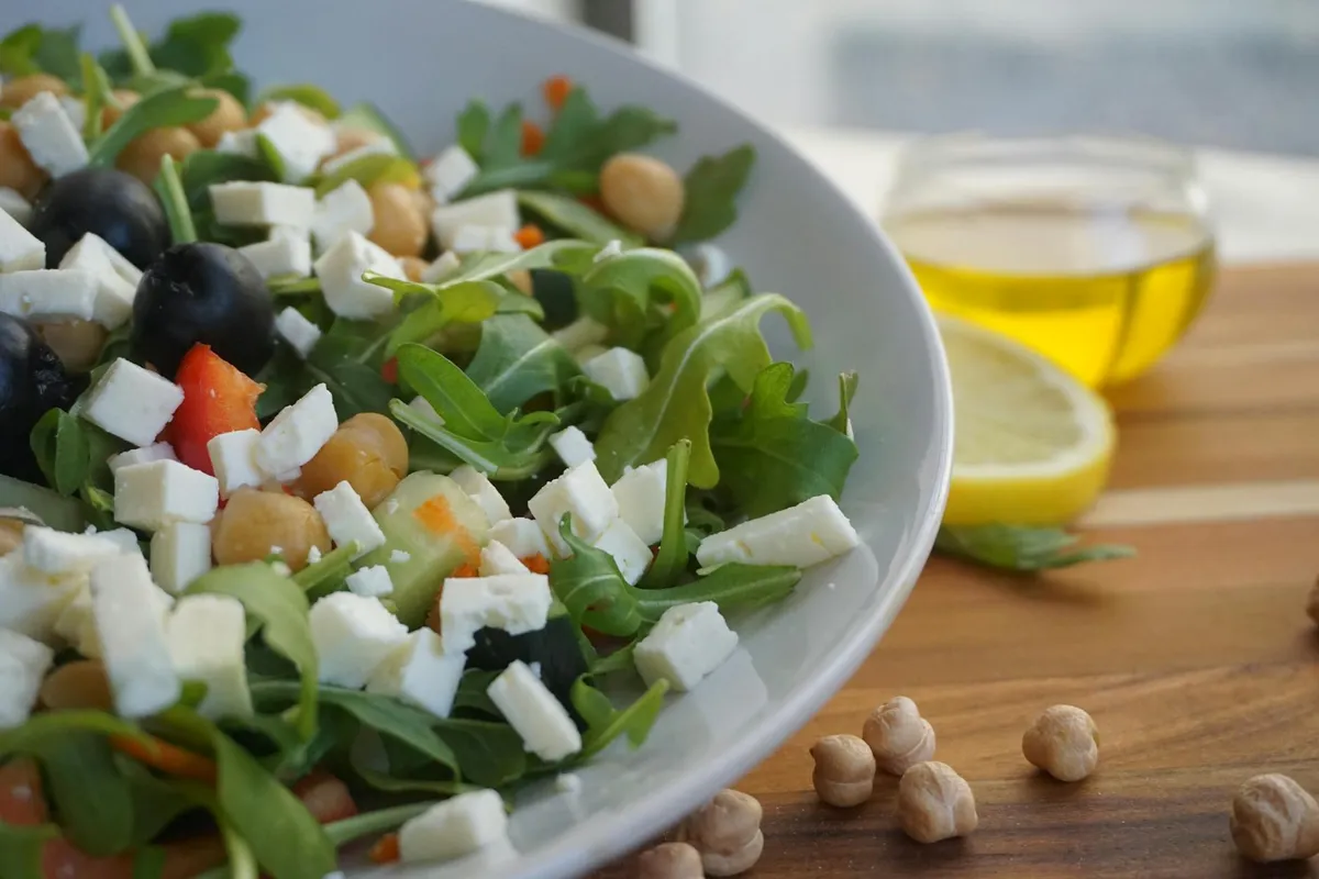 A wooden salad bowl with green leaves being drizzled with oil